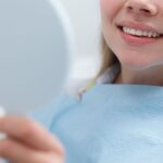 Woman examines her teeth in a hand mirror