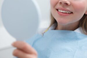 Woman examines her teeth in a hand mirror